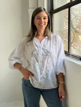 Camisa blanca de corte holgado y manga larga, con delicados bordados florales en tono gris claro en el frente.