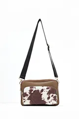 Bandolera de cuero sintético color marrón con bolsillo frontal de pelo sintético con estampado de manchas de vaca.