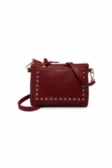 Cartera bandolera de cuero sintético color bordó, con textura craquelada, bolsillo frontal con cierre y detalles de tachas metálicas doradas. Cuenta con cierre superior y correa larga regulable y desmontable.