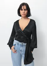 Camisa tipo blusa cruzada de seda negra, con escote en V profundo, mangas largas con puños abotonados y lazo lateral para anudar en la cintura.