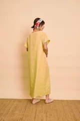 Vestido tipo túnica largo de lino color amarillo, de manga corta, con bolsillos laterales y detalle de volados en la botonera frontal.