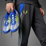 Championes de fútbol Adidas modelo F50 League FG edición Messi, con diseño en tonos plateado, azul y detalles en amarillo neón. Presenta cordones para ajuste, suela con tapones para césped natural y branding de la línea Messi.