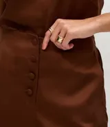 Pantalón tipo pantacourt de tiro alto, confeccionado en liocel color marrón. Presenta cierre frontal con botones forrados y elástico en la parte posterior de la cintura.
