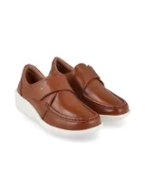 Zapato tipo slip on color camel, confeccionado en cuero con textura granulada. Presenta un diseño de mocasín con costuras reforzadas en la puntera, ajuste mediante una solapa con velcro y una suela de plataforma blanca de goma.