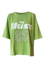Remera verde con estampado frontal con la frase "The Muse" y el número 85 en blanco y lila. De corte holgado y largo a la cadera.