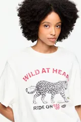 Remera oversize de algodón blanca con cuello redondo, mangas cortas amplias y estampa frontal gráfica de un leopardo con texto.