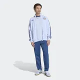 Campera deportiva Adidas Originals de la selección de Italia, color celeste con detalles en azul marino. Presenta cuello alto, cierre frontal, las icónicas tres tiras en las mangas, logo del Trifolio y escudo de la selección italiana en el pecho.