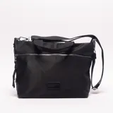 Bolso bandolera negro de material sintético, con forma rectangular y textura lisa. Posee un bolsillo frontal con cierre metálico plateado y un parche rectangular de cuero sintético en la parte inferior central. Incluye asas cortas de tela y una correa larga ajustable y desmontable.