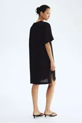 Vestido túnica de viscosa color negro, de corte holgado, largo hasta la rodilla, con cuello mao y abertura en V. Cuenta con mangas cortas, hombros caídos y aberturas laterales en el bajo.