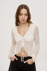 Top de encaje semitransparente color blanco, de manga larga, con escote en V pronunciado, volados en los bordes y cierre frontal con lazos para atar.