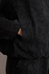Chaqueta bomber de corte recto en tejido jacquard con estampado floral en tono sobre tono negro, cuello mao y cierre frontal de broches a presión.