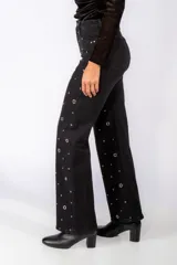 Jean de corte recto y tiro medio, color negro, con detalle de tachas metálicas circulares distribuidas por toda la prenda.