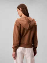 Campera canguro de felpa color marrón, con capucha ajustable con cordones, cierre frontal completo y bolsillos tipo canguro. Presenta el logo retro de Calvin Klein bordado en el pecho.