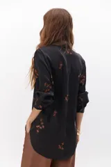 Camisa color crema de tela sedosa bordada con lentejuelas y botones negros a contratono, de corte clásico y mangas largas.