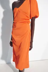 Vestido midi asimétrico de satén color naranja, con una sola manga corta abullonada, diseño drapeado en el lateral y falda cruzada.