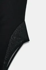 Body palabra de honor color negro, con diseño de escote corazón profundo y paneles laterales de tejido semitransparente. Confeccionado con cierre en el bajo mediante botones a presión.