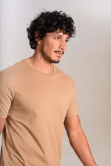 Remera de manga corta con cuello redondo, confeccionada en algodón de color beige. Presenta un pequeño logo bordado de un pingüino en el pecho.
