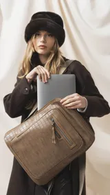 Mochila marrón con textura símil cocodrilo, compartimento principal con cierre, amplio bolsillo frontal con cierre y correas ajustables de tela.