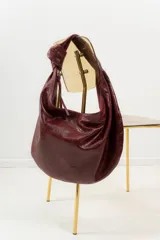 Bolso tipo hobo de cuero marrón con textura de piel de cocodrilo, asa anudada y cierre superior abierto.