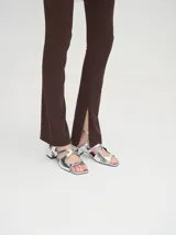 Sandalias de tacón bajo de 4.5 cm, confeccionadas en cuero con acabado de charol metalizado plateado. Presentan diseño de tiras cruzadas en el empeine, puntera cuadrada y correa ajustable al tobillo.