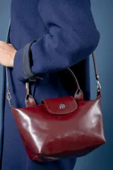Cartera pequeña de mano tipo tote, confeccionada en gamuza color azul, con solapa y asas en cuero sintético con textura de reptil. Incluye cierre superior y correa larga ajustable y extraíble.