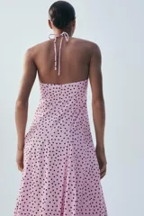 Vestido midi de color rosado con estampado de lunares negros, cuello halter con tirantes finos ajustables, escote recto y diseño fluido con volumen.