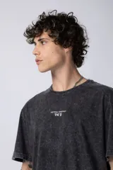 Remera de corte holgado con efecto de lavado ácido en tono gris oscuro. Presenta un pequeño estampado gráfico en el centro del pecho con la inscripción 'ASTRAL ENERGY' y las siglas 'VCP'.