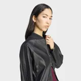Campera Adidas estilo bomber de efecto piel color negro, de corte holgado, con cierre frontal de cremallera y diseño urbano.