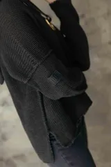 Sweater de punto negro con capucha, diseño de manga larga y corte holgado. Presenta un detalle de argolla metálica en el escote.