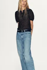 Polo negro de punto calado con cuello clásico, manga corta abullonada y terminación ondulada en el ruedo.