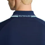 Campera deportiva adidas de la selección de Alemania, color azul marino con detalles en celeste. Presenta cierre frontal, cuello tipo polo, bolsillos laterales y las icónicas tres tiras de la marca en las mangas. Incluye el logo del trébol de adidas y el escudo de la federación alemana de fútbol en el pecho.