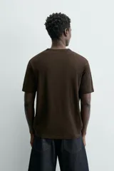 Camiseta de corte relajado (relaxed fit) color blanco roto o crema, con cuello redondo y manga corta.