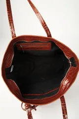 Bolso tipo shopper marrón con textura efecto cocodrilo y acabado charol, de gran tamaño y estructura semirrígida. Cuenta con doble asa de hombro y un pequeño estuche colgante desmontable.