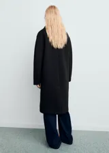 Abrigo largo de corte recto y diseño combinado, con cierre de doble botonadura, cuello camisero y dos bolsillos laterales. Cuenta con forro interior y manga larga.
