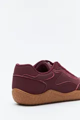 Zapatilla de estilo barefoot color marrón, confeccionada con una combinación de gamuza y materiales sintéticos. Presenta un diseño de perfil bajo con suela de goma flexible en color caramelo que incluye el logo de la marca grabado en el lateral.