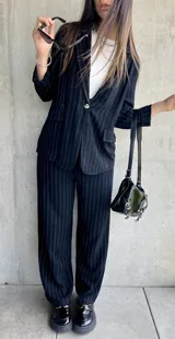 Blazer negro con finas rayas verticales blancas, solapas de muesca, cierre frontal con un botón y bolsillos laterales.