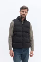 Chaleco puffer negro con diseño matelaseado, cierre frontal completo y cuello alto. Cuenta con bolsillos laterales y un pequeño parche con logo en el pecho.