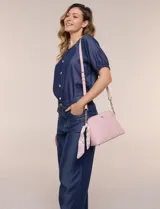 Cartera bandolera estructurada de eco cuero rosado con textura graneada, silueta curva y cierre superior. Posee correa larga regulable con detalles de cadena dorada, bolsillo frontal con logo metálico, pañuelo estampado a contratono anudado en un lateral y base rígida con apoyos metálicos.