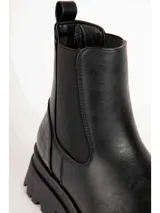 Bota de caña baja tipo Chelsea color marrón, con paneles elásticos laterales y suela track negra con plataforma dentada. Presenta textura en relieve en la parte trasera del talón.