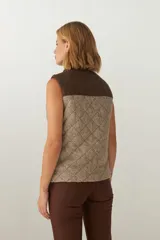 Chaleco de lana fina sin teñir con diseño acolchado en rombos y canesú en contraste. Cuenta con cuello alto, cierre frontal de cremallera y bolsillos laterales.
