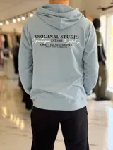 Canguro celeste con capucha, sin felpa y de diseño liviano, con estampado tipográfico en la espalda en color negro y blanco.