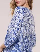 Blusa azul y blanca con estampado floral y geométrico, de calce suelto, con escote redondo, abertura tipo keyhole en el pecho, mangas tres cuartos y ruedo amplio con silueta evasé.