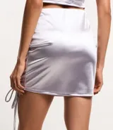 Minifalda color lila de satén con fruncido lateral y cordones ajustables.