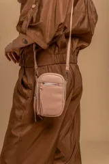 Bandolera compacta color rosado, con correa regulable y desmontable. Tiene apertura superior, bolsillo frontal con cierre y detalle de borla, y bolsillo trasero sin cierre. El interior está forrado en tela y cuenta con un bolsillo adicional.