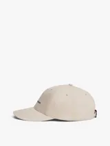 Gorra de seis paneles color beige claro, confeccionada en algodón, con visera curva rígida y ojales bordados. Presenta el logo de Tommy Hilfiger bordado en el panel frontal.