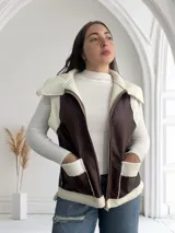 Chaleco marrón de ecocuero con interior de corderito blanco, cierre frontal con cremallera y bolsillos laterales.
