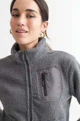 Campera negra de corderito con cuello alto, cierre frontal con cremallera, bolsillo de parche en el pecho y bolsillos laterales.