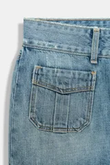 Falda mini de denim azul claro, tiro medio, con bolsillos de plastrón delanteros y cierre frontal con botones metálicos.