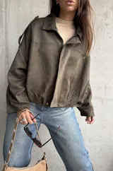 Campera tipo bomber de gamuza color verde, con diseño oversize, cuello camisero, cierre frontal y detalles de charreteras en los hombros.
