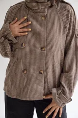 Chaqueta de corte estructurado con estampado cuadrille en tonos marrones y beige. Presenta cuello alto con tira ajustable, cierre frontal con botones, charreteras en los hombros y puños con detalle de hebilla.
